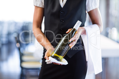 Mid section of waitress holding a bottle of white wine and a towel