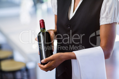 Mid section of waitress holding a bottle of red wine and a towel