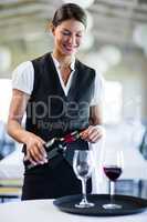 Smiling waitress pouring red wine in a glass