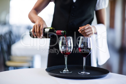 Mid section of waitress pouring red wine in a glass