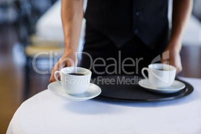 Mid section of waitress serving cup of coffee