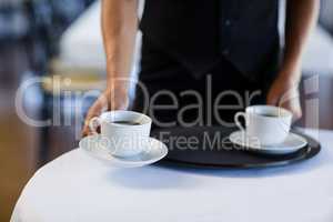 Mid section of waitress serving cup of coffee