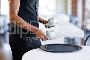 Mid section of waitress serving cup of coffee
