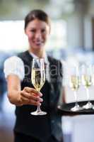 Portrait of smiling waitress offering a glass of champagne