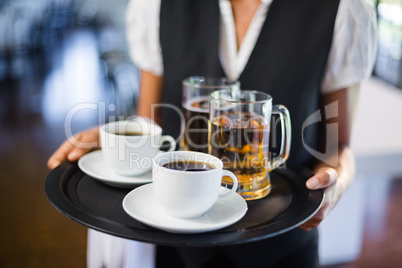 Mid section of waitress holding serving tray with coffee cup and pint of beer