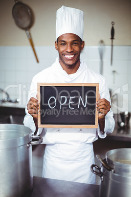 Smiling chef showing chalkboard with open sign