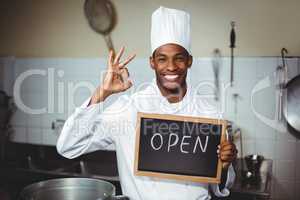 Smiling chef showing chalkboard with open sign