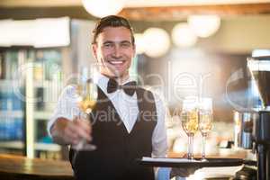 Portrait of smiling waiter offering a glass of champagne