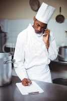 Chef writing on clipboard while talking on phone