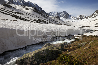 River with snow bridges in spring mountains at sun day
