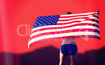 Rear view of sportsman is raising an american flag  against blur