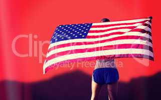 Rear view of sportsman is raising an american flag  against blur