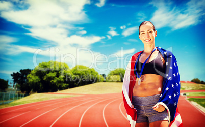 Sporty woman posing and smiling with American flag against athle