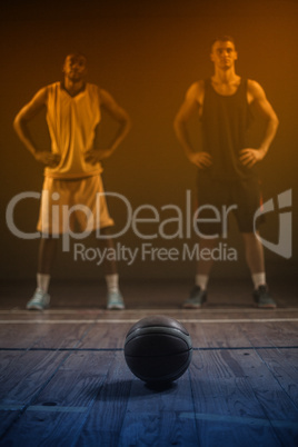 Basketball players posing with hands on hips behind a ball