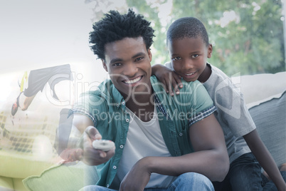 Composite image of father and son watching tv together on the co