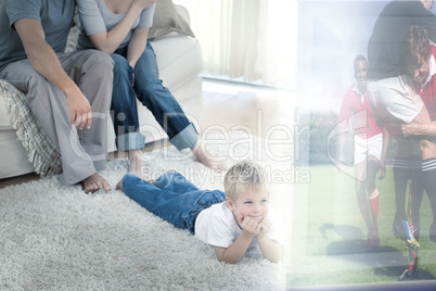 Composite image of cute boy lying on carpet is watching sport on