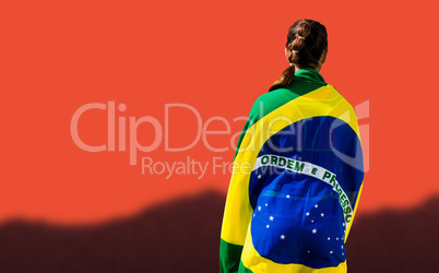 Rear view of sporty woman holding the Brazilian flag against blu