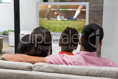 Composite image of happy family watching tv on the sofa