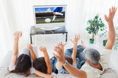 Composite image of family raising their arms in front of televis