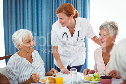 Smiling nurse looking at senior person during breakfast