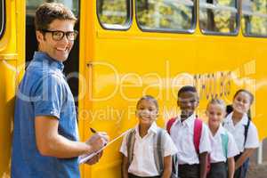 Smiling teacher updating check list of kids while entering in bu