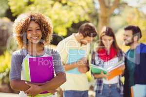 Portrait of college girl holding notes with friends in backgroun