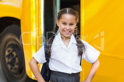 Smiling schoolgirl standing in front of school bus