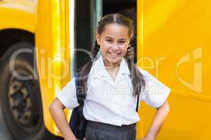 Smiling schoolgirl standing in front of school bus