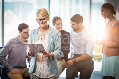 Businesswoman using digital tablet while coworker interacting in