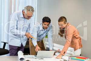 Businesswoman and coworkers discussing blueprint using laptop
