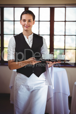 Portrait of smiling waitress holding a tray of coffee cups