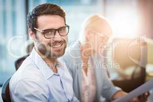 Man smiling at camera while his colleague reading document