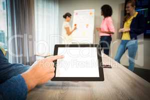 A colleague using digital tablet while coworkers discuss flowcha