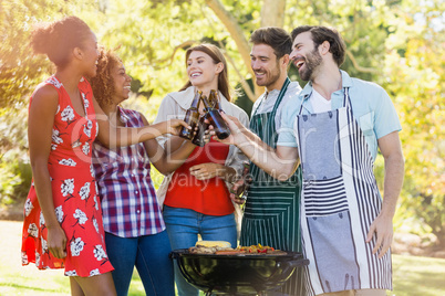 Group of friends toasting a beer bottle while preparing barbecue