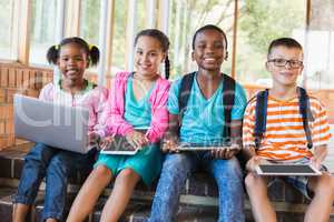 Portrait of kids using a laptop and digital tablet on stairs