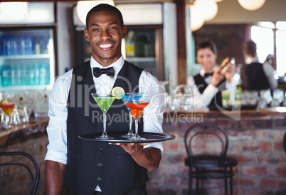 Portrait of bartender holding serving tray with cocktail glasses