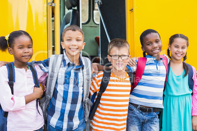 Smiling kids standing arm around in front of school bus