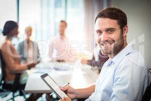 Man holding digital tablet while coworker interacting in the bac