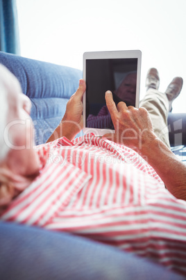 Lying on a couch senior man touching digital tablet