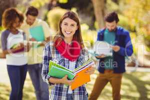 Portrait of college girl holding notes with friends in backgroun