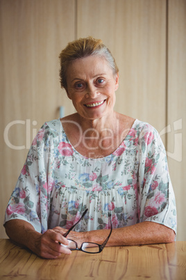 Smiling senior woman holding glasses seated on a table