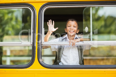 Smiling schoolboy waving hand from bus