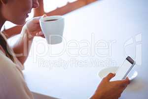 Woman using smartphone and drinking coffee