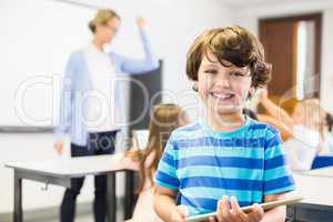 Portrait of schoolboy holding digital tablet in classroom