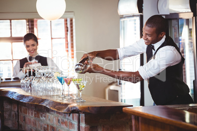 Bartender pouring a drink from a shaker to a glass on bar counte