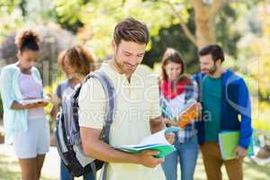 College boy reading notes with friends in background