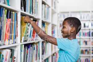 Schoolboy selecting a book from bookcase in library