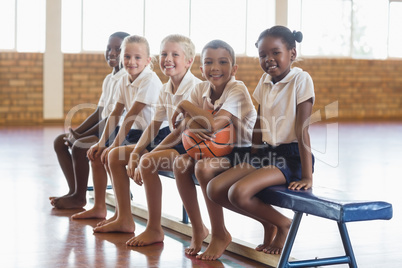 Smiling students sitting on bench with basketball