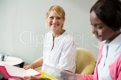 Woman smiling at camera while her colleague reading document