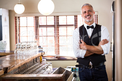 Portrait of smiling bartender standing with arms crossed